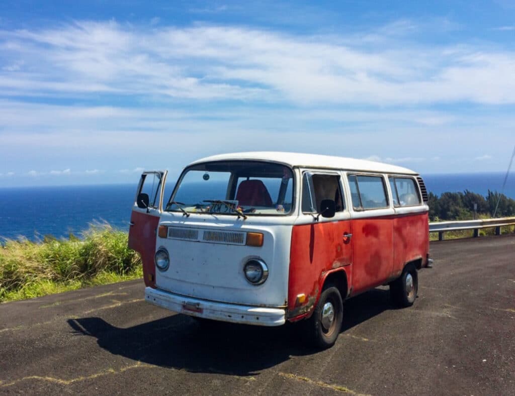 A vintage red VW bus in front of the beautiful Kohala Coastline on a road trip to Waipio Lookout