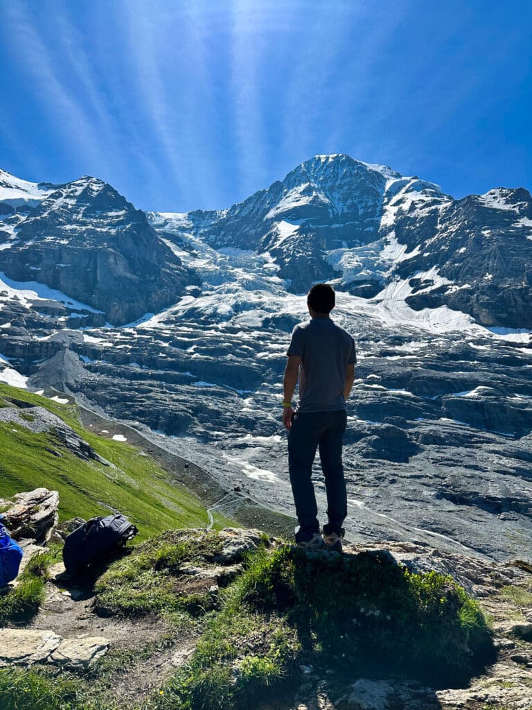Hiker standing on rocky terrain with views of the Eiger’s North Face and the Eiger Glacier near Kleine Scheidegg
