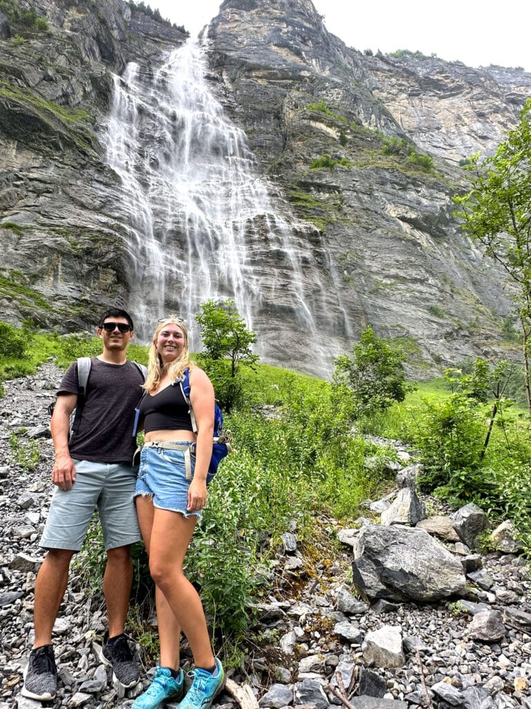 Two hikers standing at the base of a waterfall along the Lauterbrunnen Valley walking trail