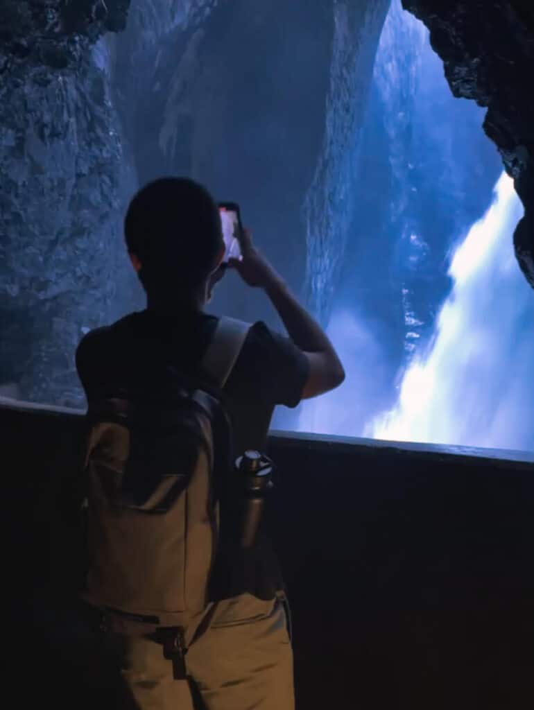 Visitor standing inside Trümmelbach Falls cavern, looking out at powerful waterfall pouring through the mountain