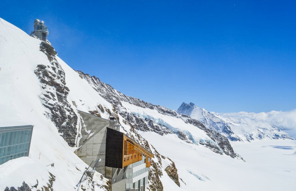 A breathtaking view of a mountain observatory against a clear blue sky, surrounded by snow-covered peaks.