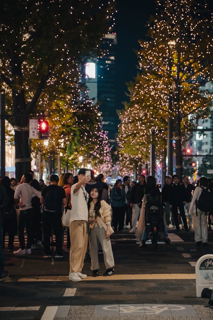 A couple takes a selfie surrounded by festive lights on a bustling Osaka street at night.