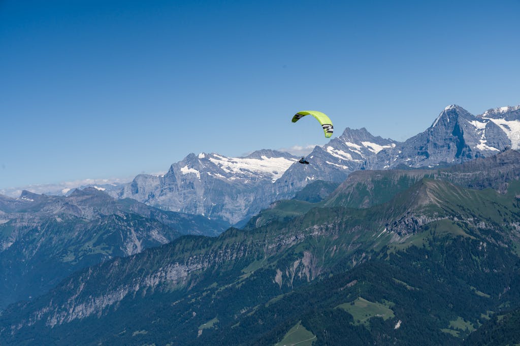 A paraglider soars over the scenic Swiss Alps with clear blue skies in summer.