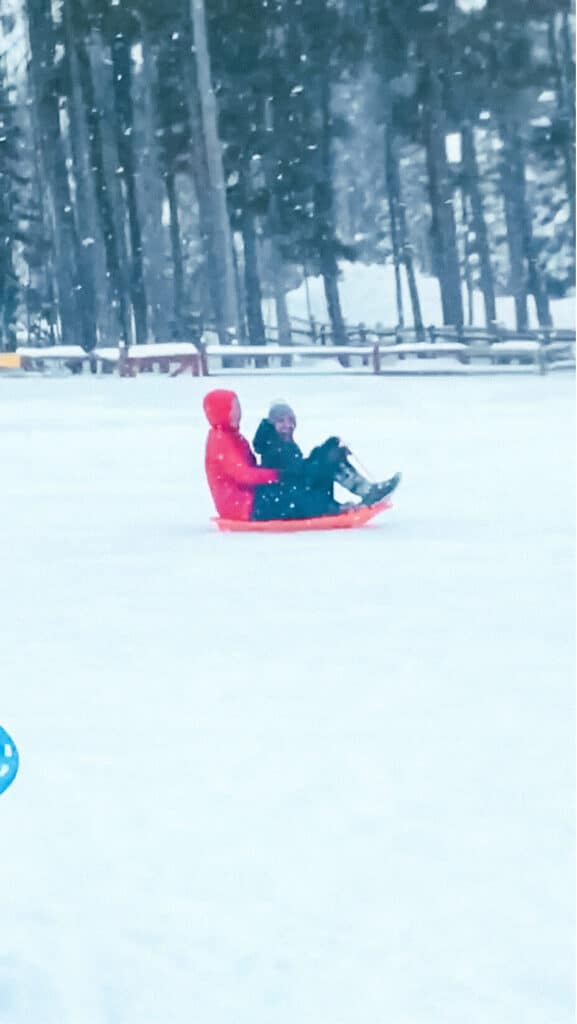 Two friends riding a sled downhill in deep snow at Breckenridge’s public sledding hill.