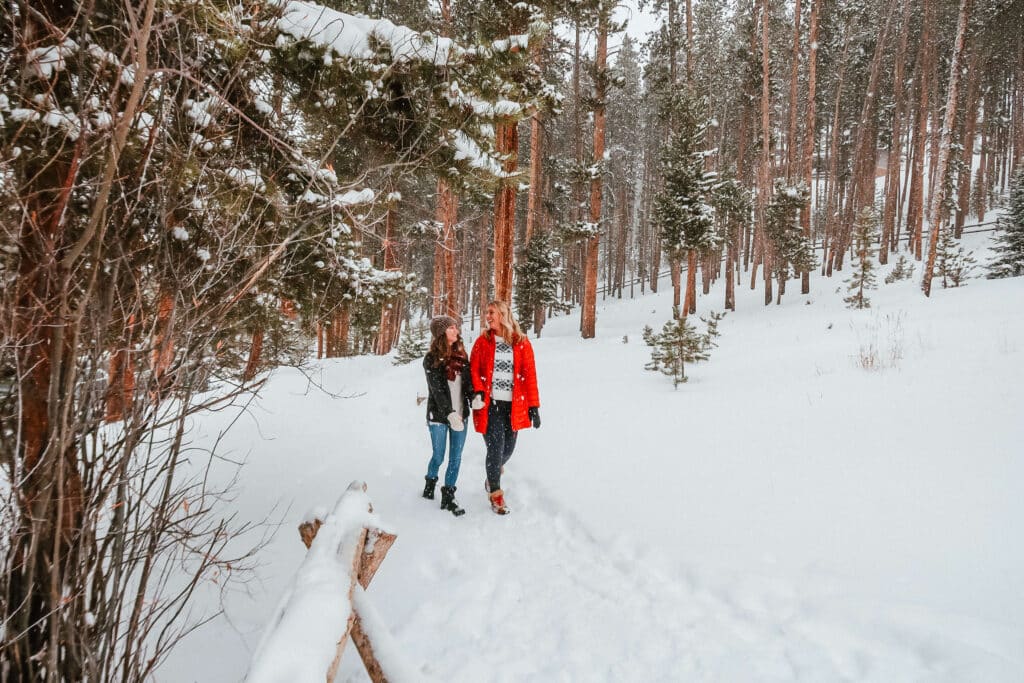 Friends hiking through snow-covered woods with footprints trailing behind.