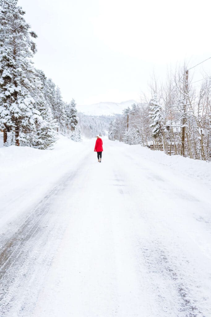 A solo figure walking down a snow-covered road flanked by pine trees near Breckenridge.