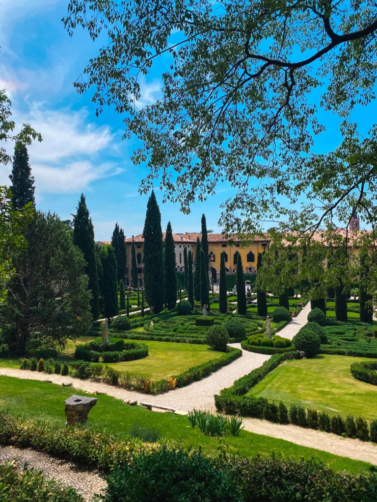 Manicured hedges and winding paths in the lower formal garden at Giusti Garden in Verona, with towering trees framing a bright blue sky