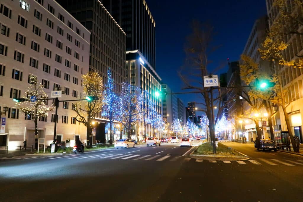 A city street in Japan lined with bright Christmas lights and illuminated buildings on a winter night.