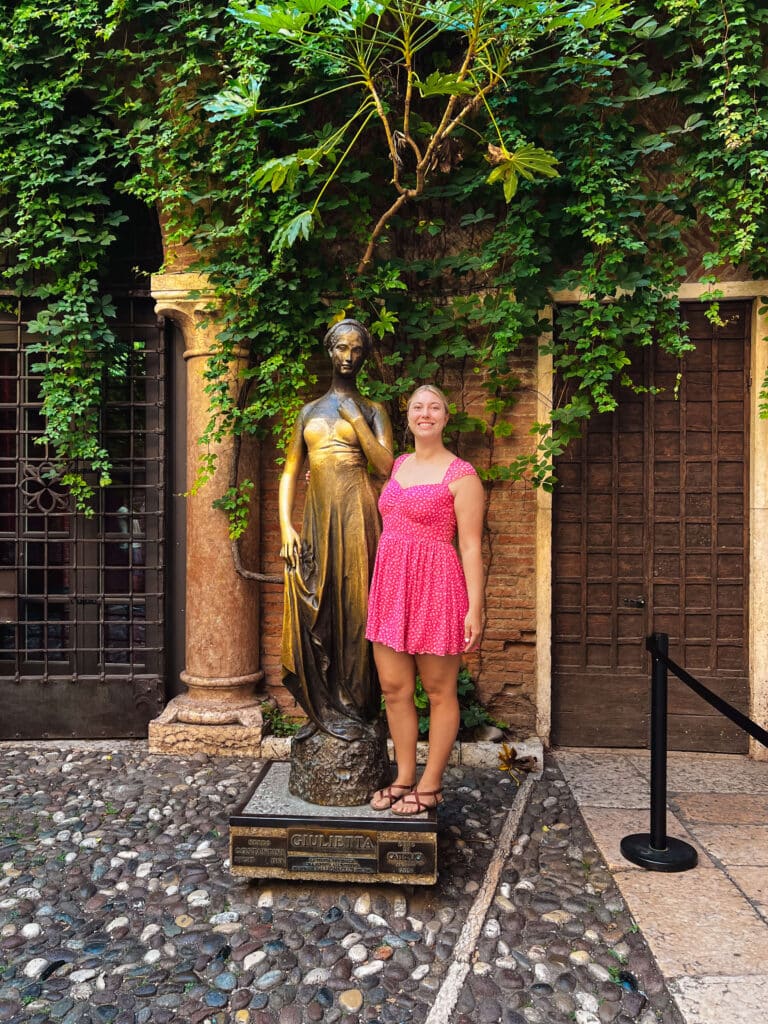 A happy tourist posing with the bronze statue of Juliet from Romeo & Juliet at the Casa di Giuliette Museum in Verona