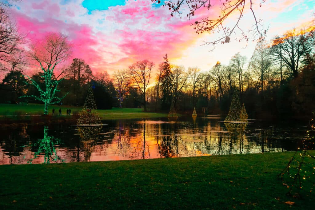 Twilight view of a colorful holiday sunset over a reflecting pond and light-wrapped trees at Longwood Gardens.