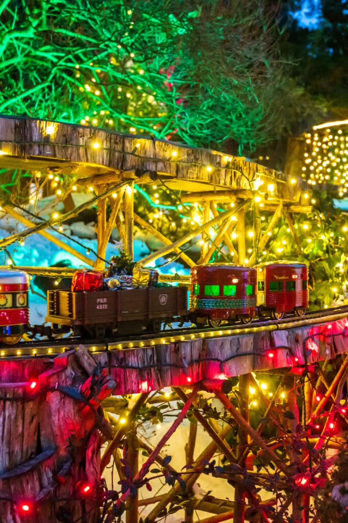 Holiday model train display at Morris Arboretum, surrounded by glittering lights and miniature village structures.