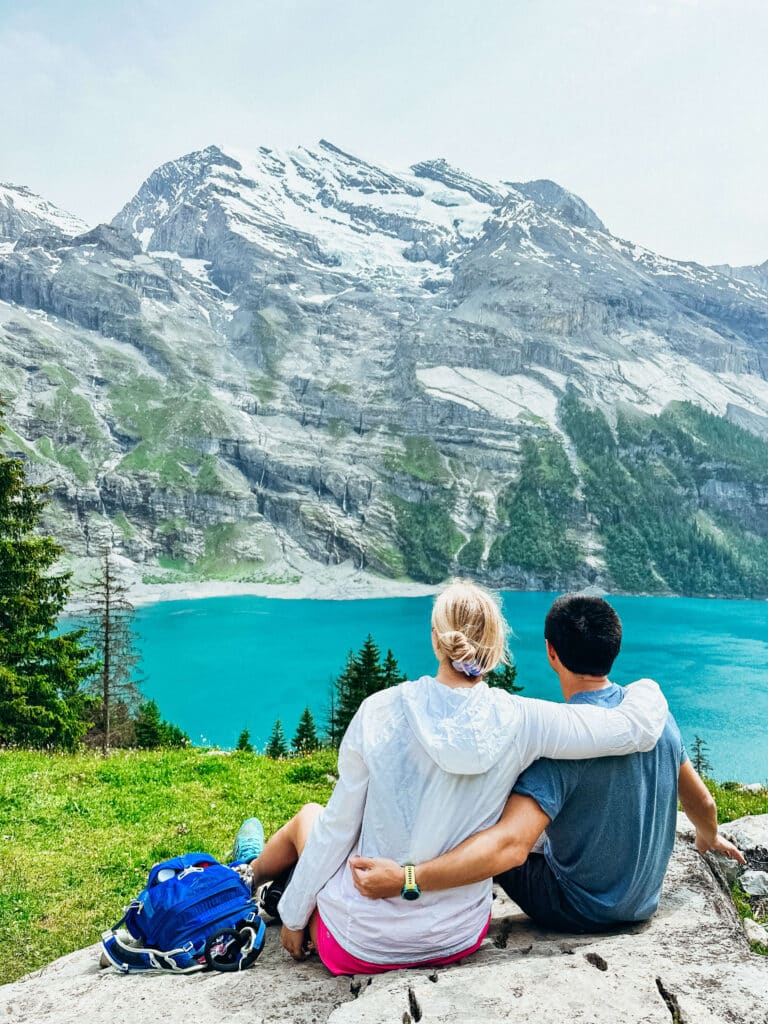 Two people sitting on a rock in front of blue water at Oeschinensee Lake