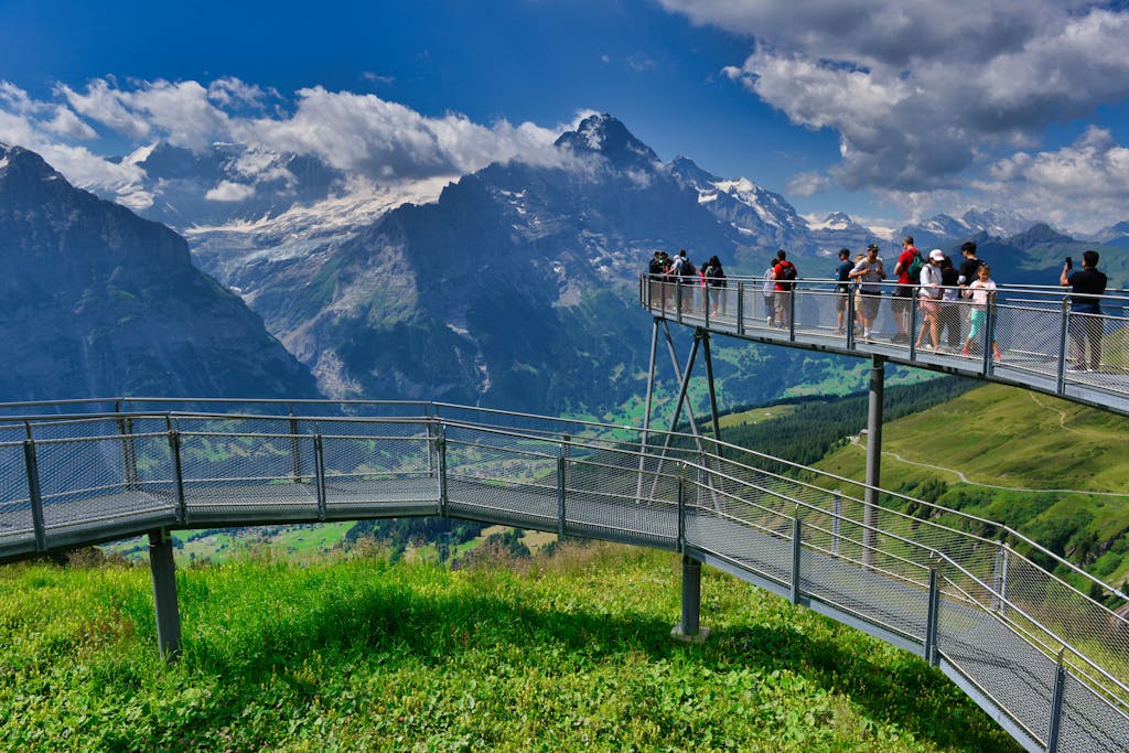 Panoramic view of Grindelwald, Switzerland with tourists on a scenic bridge against majestic mountains.