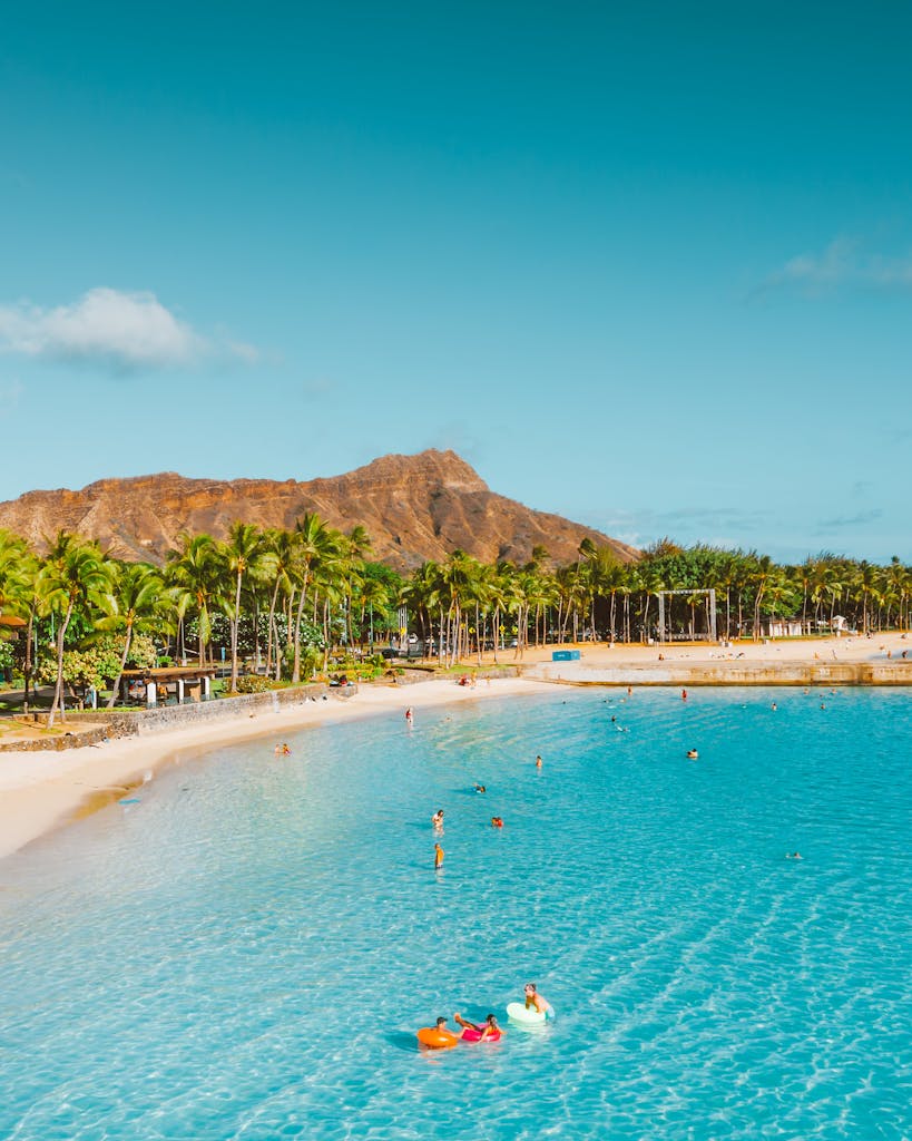Relaxing tropical beach with turquoise waters, palm trees, and a mountain backdrop.