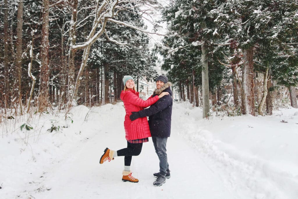 A snowy forest trail in Hakuba Japan with two travelers embracing, surrounded by white winter scenery.