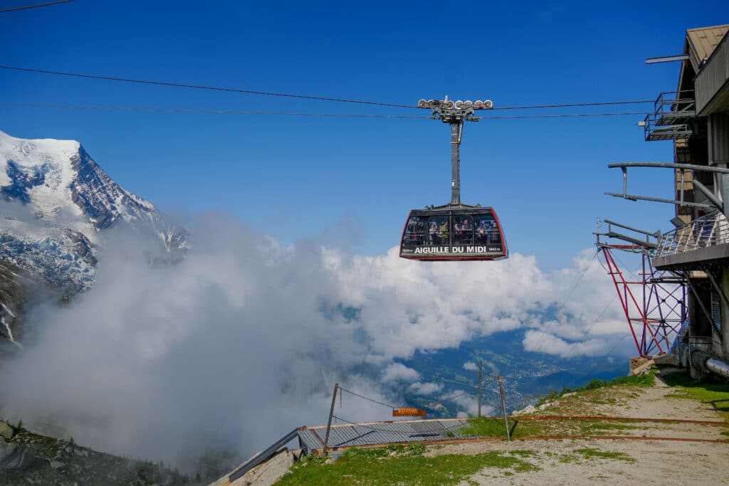 The Aiguille du Midi gondola at the mid station at Plan d'Aiguille in front of blue skies and puffy clouds