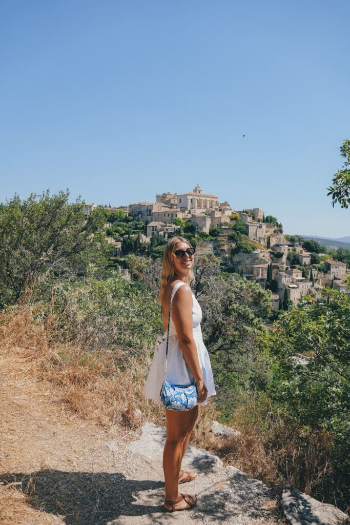 Traveler standing at a rocky viewpoint overlooking Gordes, Provence, with the village rising in the distance.