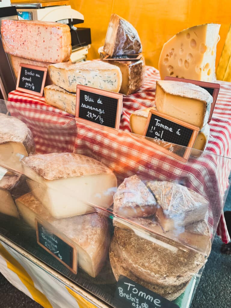 French cheese stall with labeled wedges and rounds at a local Provençal market.