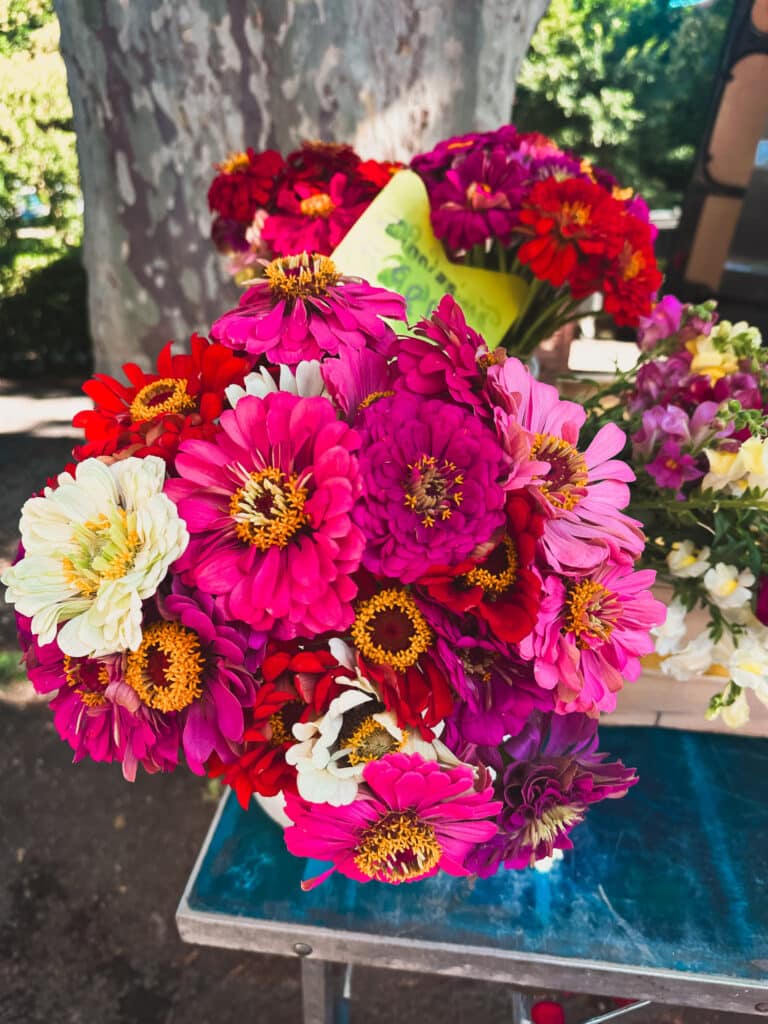 Bright bouquet of zinnias and summer flowers for sale at a Provençal market stall.