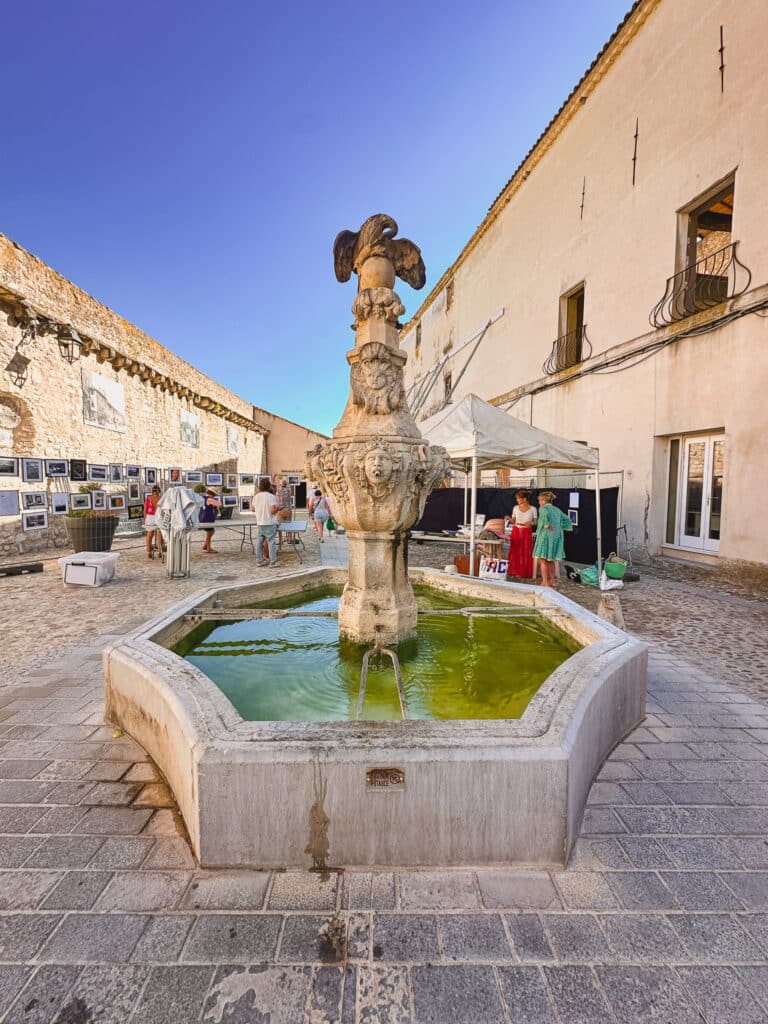 Stone fountain bubbling in a sunlit square in Pernes-les-Fontaines, Provence.