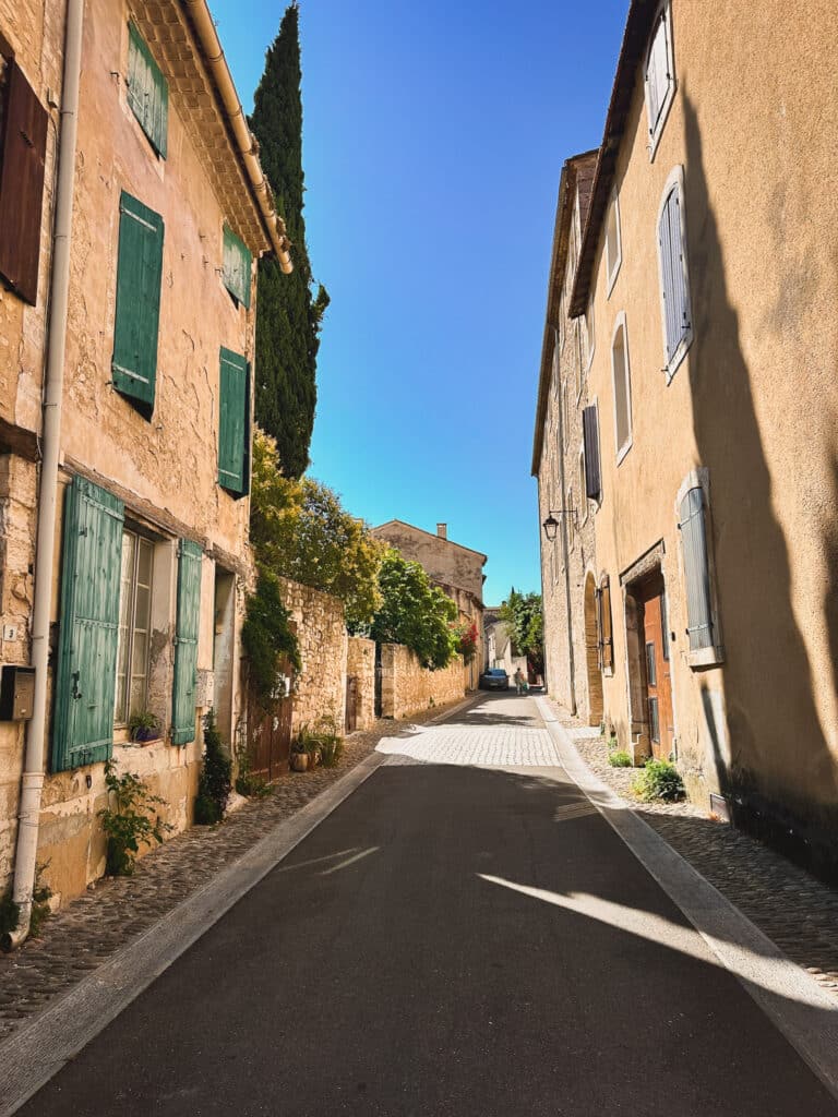 Narrow sunlit street lined with stone buildings in Pernes-les-Fontaines, Provence.