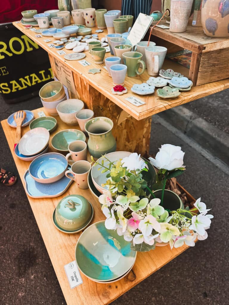 Handmade ceramics arranged on a wooden table at the Pernes-les-Fontaines market.