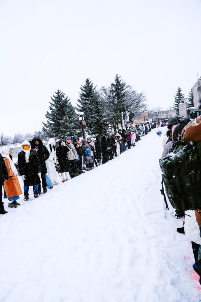 Crowd gathered behind the route as penguins approach through falling snow.