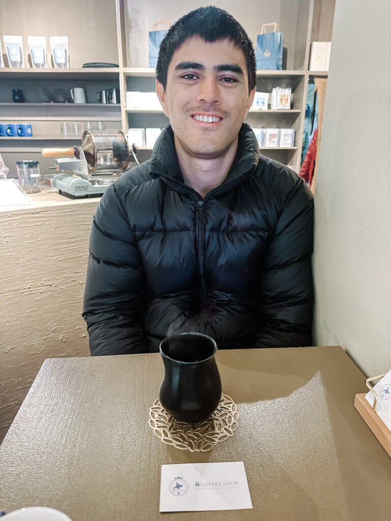 Travel Buddy seated at a café table in Sapporo with a freshly served coffee.