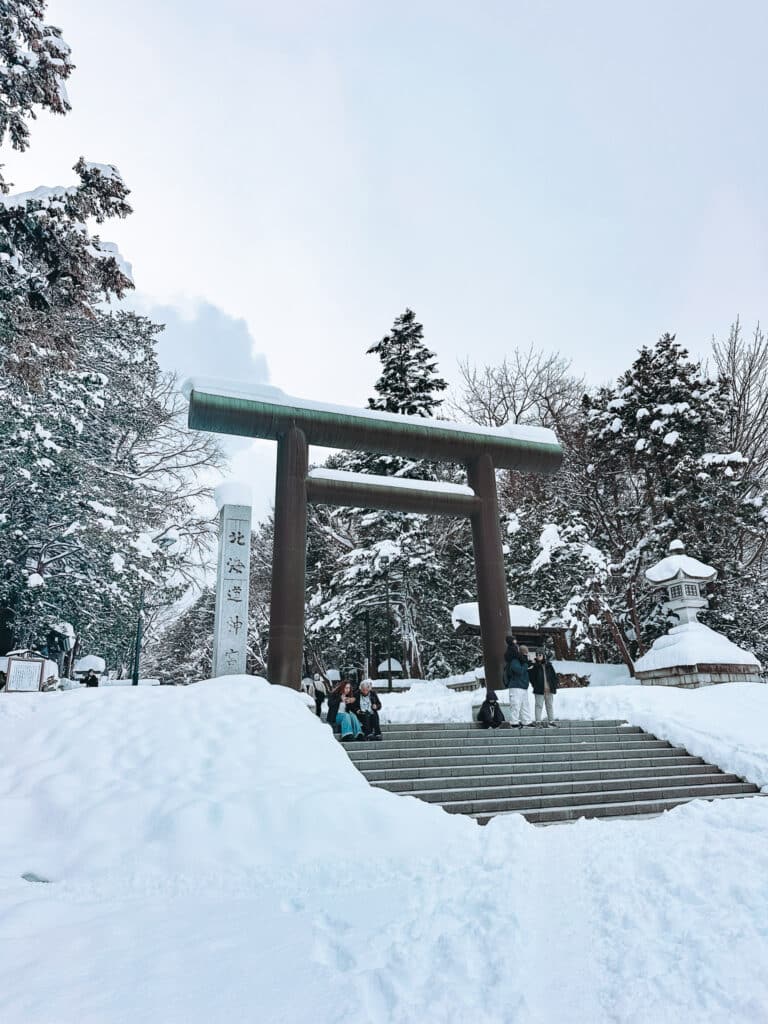 Snowy torii gate at Hokkaido Jingu with stone steps and frosted trees behind.