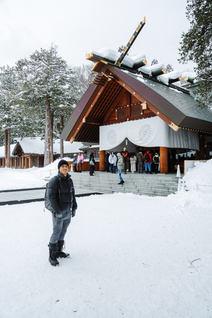 Visitor walking toward Hokkaido Jingu’s main hall across a snow-covered courtyard.