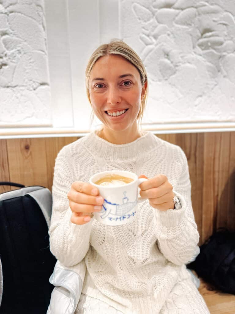 Traveler holding a latte and smiling inside a Sapporo Mermaid Coffee Roasters coffee shop