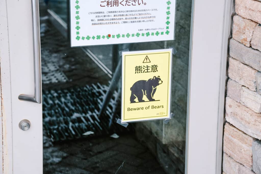 Yellow “Beware of bears” warning sign posted on a glass door at Mt. Moiwa.