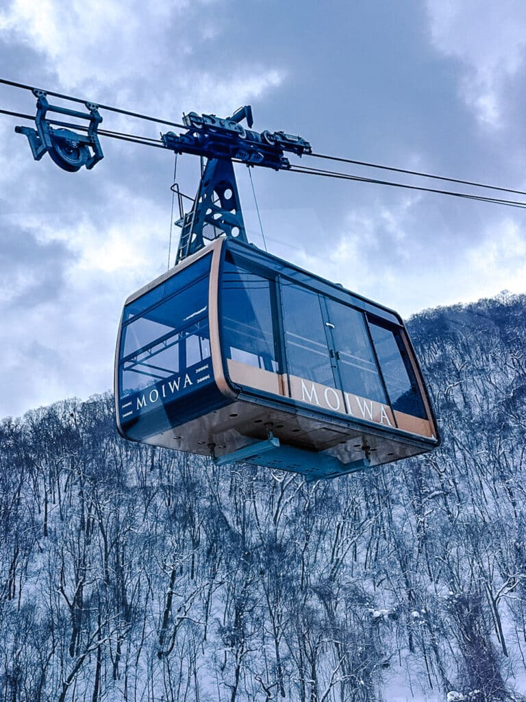 Mt. Moiwa ropeway gondola car suspended over a snowy, tree-covered mountainside.