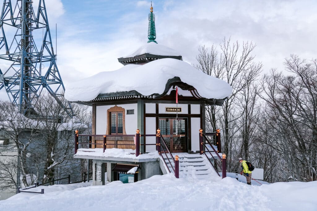 Small shrine-like building at Mt. Moiwa summit surrounded by snow and ropeway towers.
