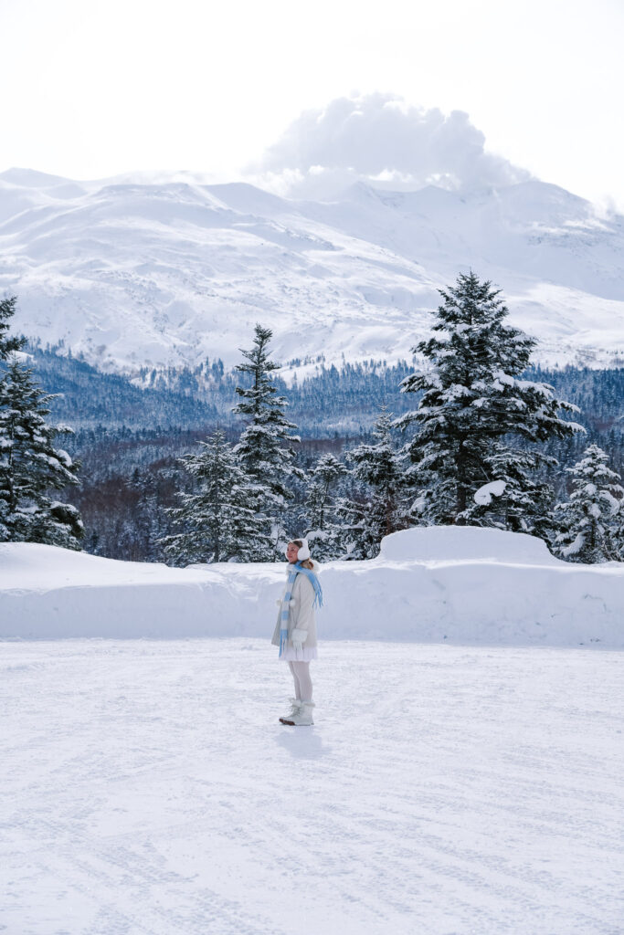 Traveler in a snowy field with volcanic mountains near Shirogane Onsen, Hokkaido, Japan.