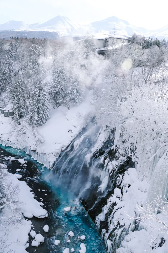 Vertical view of Shirahige Waterfall with steam rising into cold air above the blue river, Hokkaido.