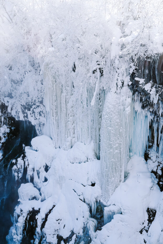 Frozen cliffside at Shirahige Waterfall with thick icicles and snow buildup, Hokkaido, Japan.