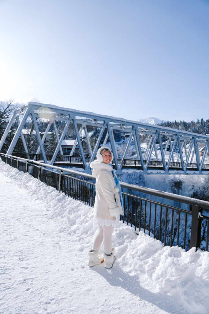 Traveler standing beside the railing on Shirogane Blue River Bridge near Shirahige Waterfall, Biei, Hokkaido.