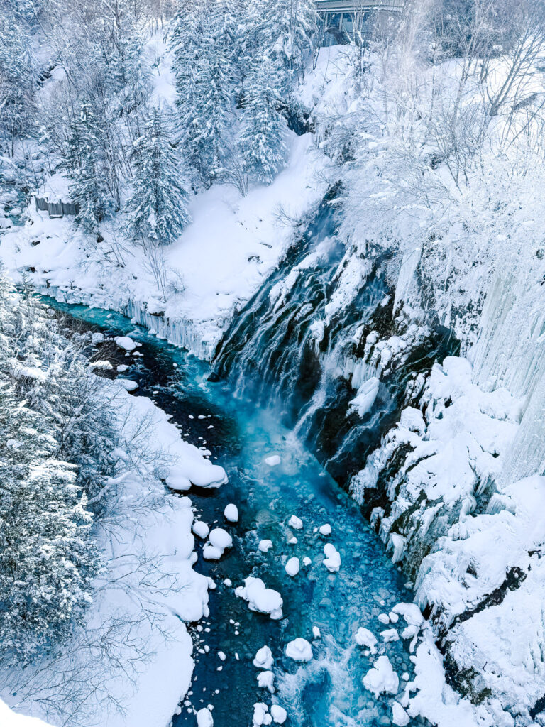 Shirahige Waterfall and vivid blue river cutting through a snowy gorge, partially frozen in winter, Hokkaido.