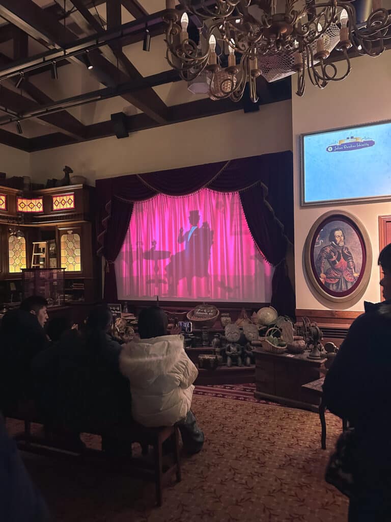 Visitors seated in a small theater watching a pink-curtained stage and screens during the CHOCOTOPIA chocolate show.