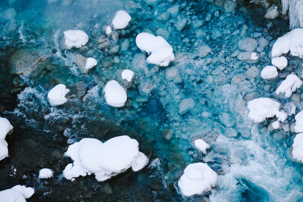 Close-up of electric-blue river water with snow-capped rocks near Shirahige Waterfall, Hokkaido.