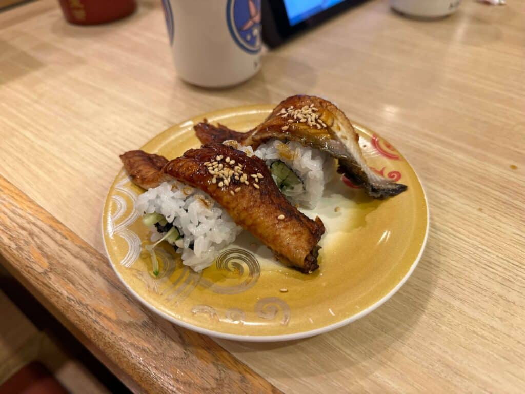 Close-up of a yellow plate of eel sushi topped with sesame seeds at Toriton Maruyama in Sapporo.