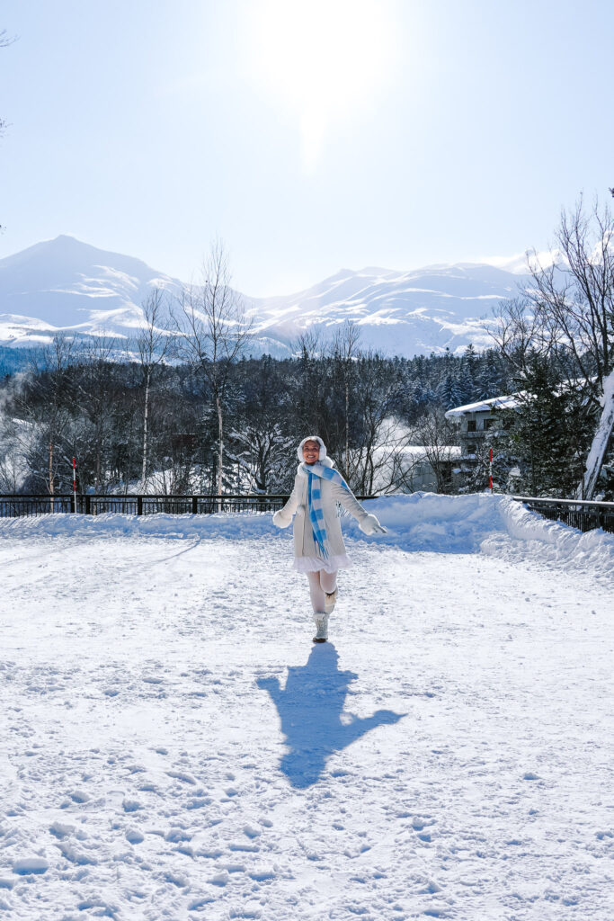 Traveler in a snowy field with volcanic mountains near Shirogane Onsen, Hokkaido, Japan.