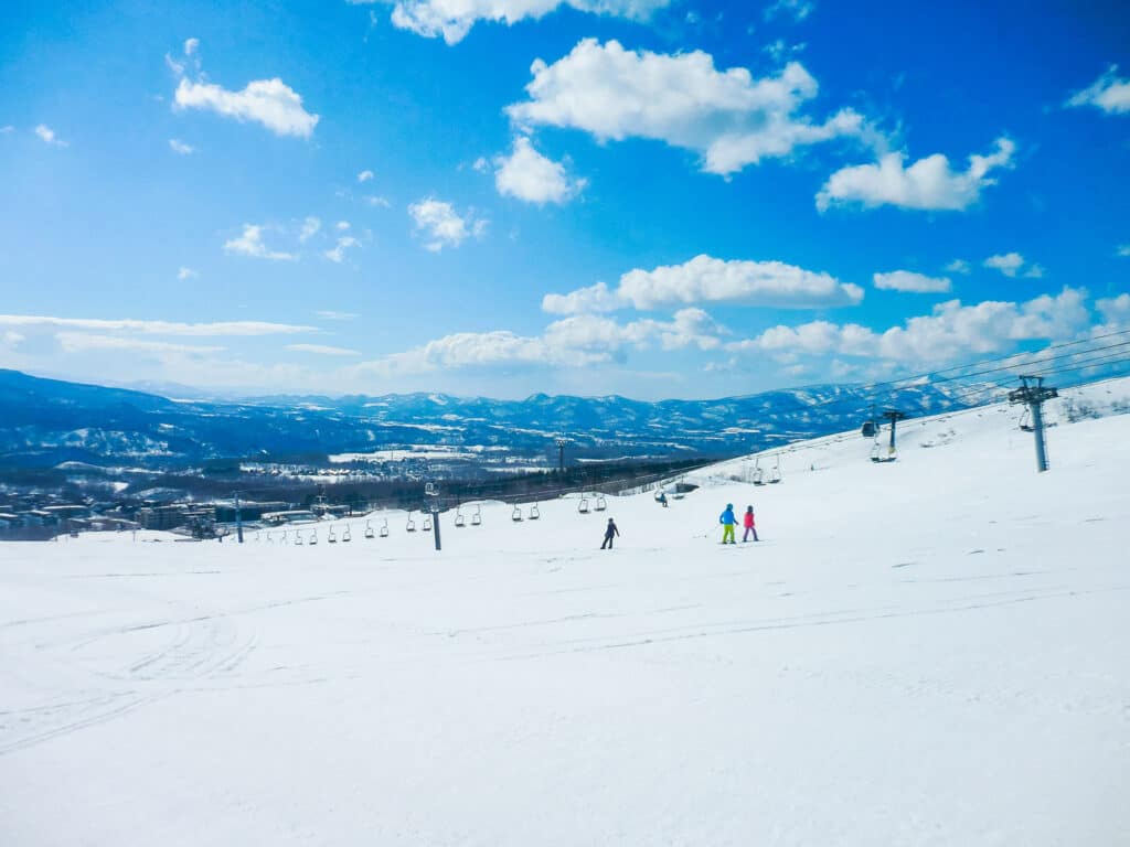 Wide ski slopes at Niseko in Hokkaido with little figures flying down on the snow
