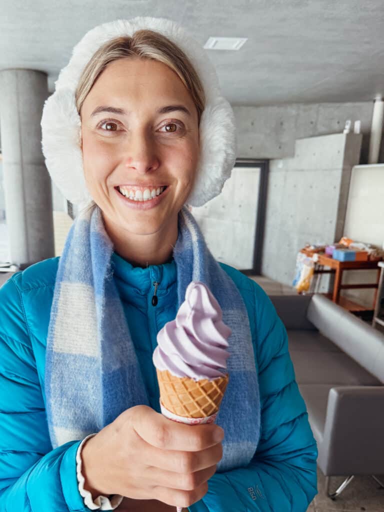 A traveler holding a waffle cone with a spiral of purple lavender ice cream soft serve at the Hill of the Buddha in Sapporo