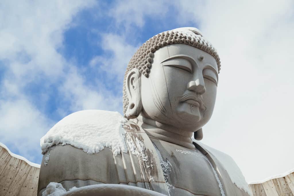 Close-up of the Buddha statue at the Hill of the Buddha in Sapporo with melting snow running down the stone face.