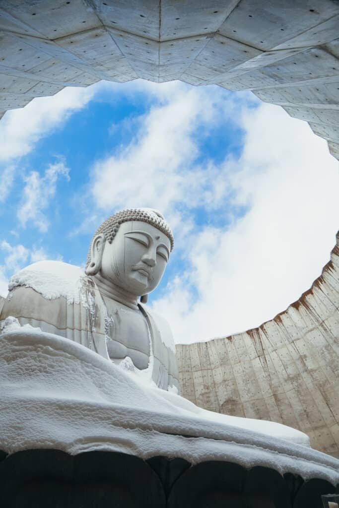 Low-angle view of the massive Buddha statue framed by the circular concrete rotunda at the Hill of the Buddha in Sapporo.