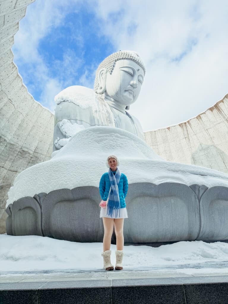 Visitor standing in front of the giant Buddha statue inside the Hill of the Buddha rotunda in Sapporo.