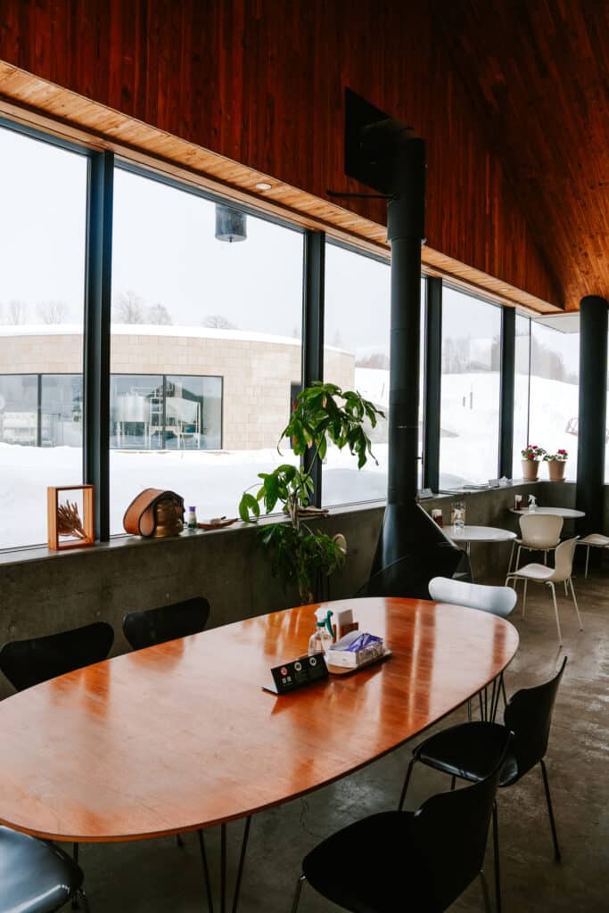 Warm interior of La Laiterie cafe with wooden tables, large windows, and views of the snowy farm
