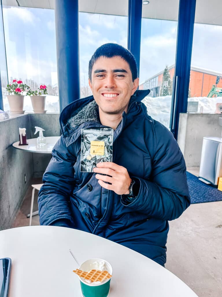 Man holding a package of cheese cubes inside La Laiterie cafe in Biei, Hokkaido, with a dessert on the table